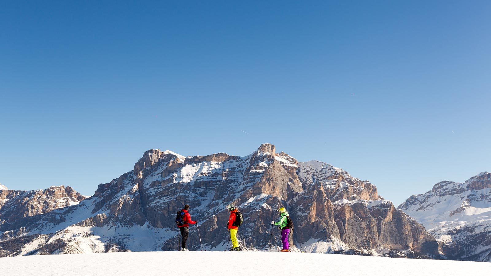 Three skiers admire the Dolomites on a sunny winter day